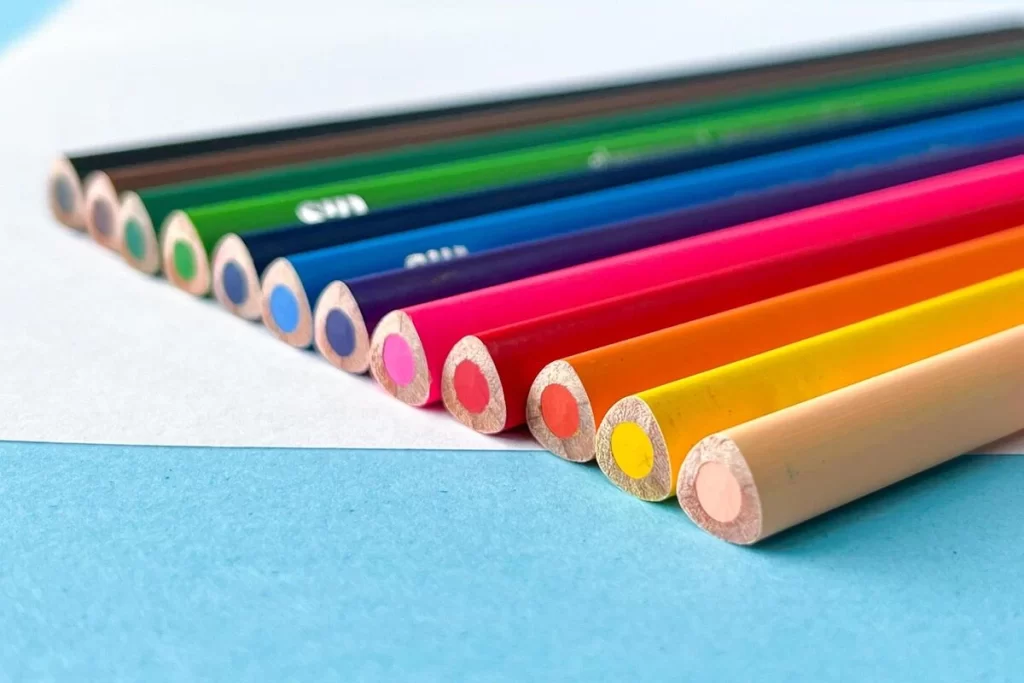Foto de lápis de cor coloridos em linha, destacando tons vibrantes como pink, amarelo, azul e verde, sobre um fundo azul.