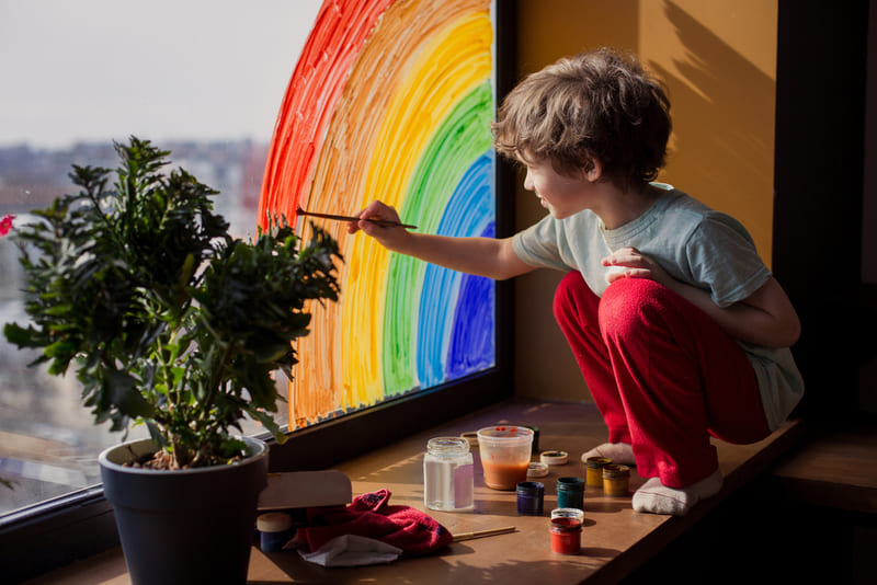 menino pintando um arco-íris na janela