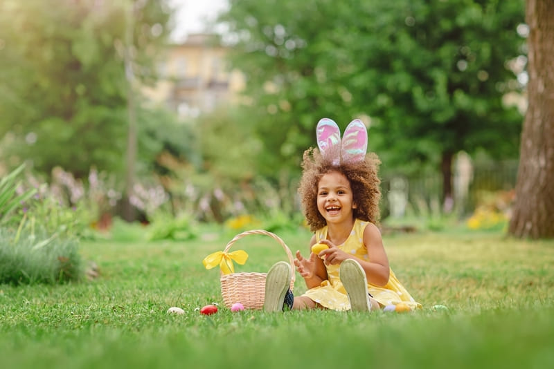 Menina brincando com cesta de ovos de Páscoa em área verde