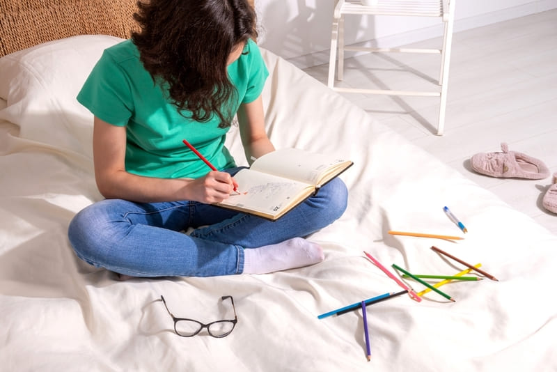 Adolescente sentada na cama pintando agenda com lápis de cor
