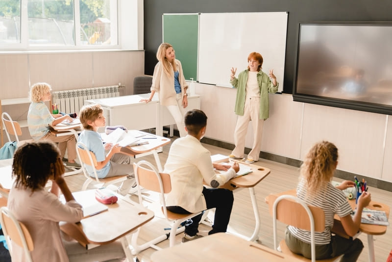 Menina apresentando trabalho em sala de aula para professora e colegas