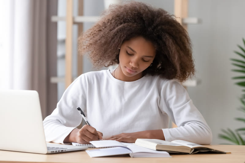 Adolescente concentrada estudando com livros e notebook