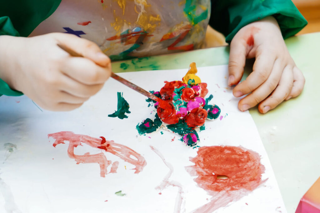 Criança pintando flor com tinta guache.