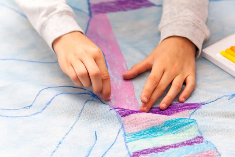 Criança desenhando com giz pastel em um grande papel.