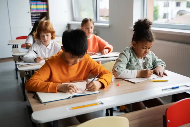 Crianças em uma sala de aula concentradas em atividades de escrita, desenvolvendo habilidades escolares essenciais em um ambiente educativo.