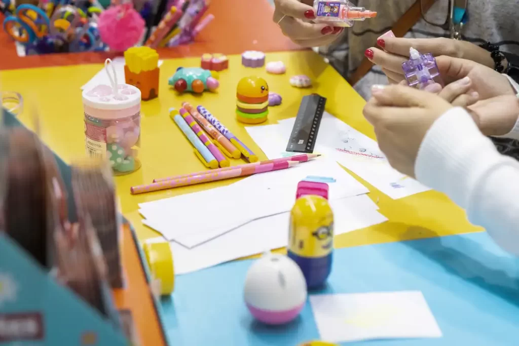 Pessoas testando materiais de arte e escolares da Tris, incluindo canetas coloridas, adesivos e produtos decorativos.
