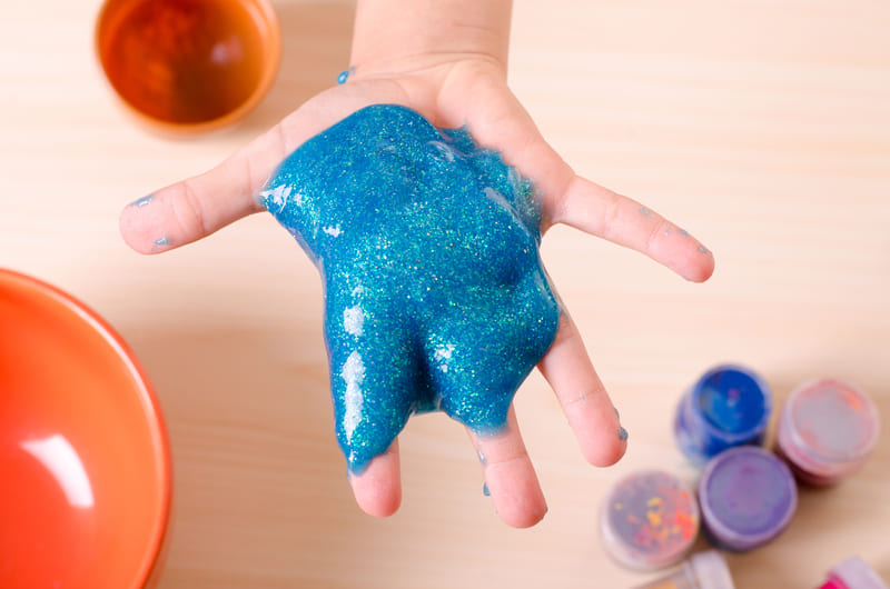 Mão de criança segurando slime azul com glitter