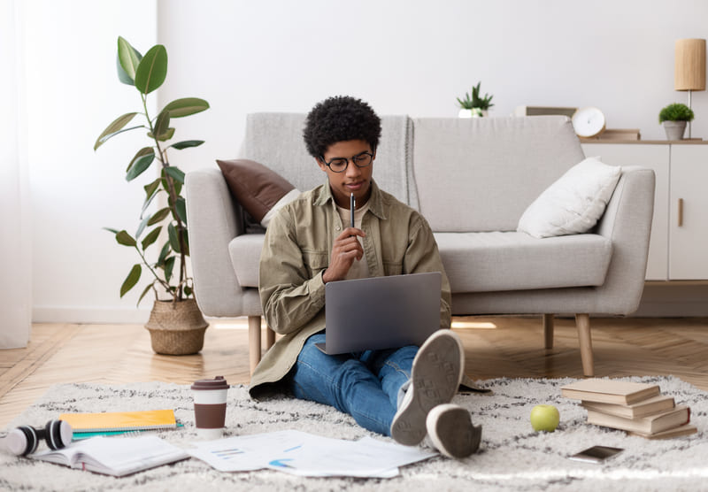 Jovem sentado no chão estudando com o notebook no colo