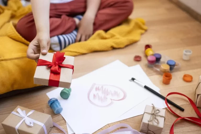 Criança sentada no chão pintando e segurando presente de natal