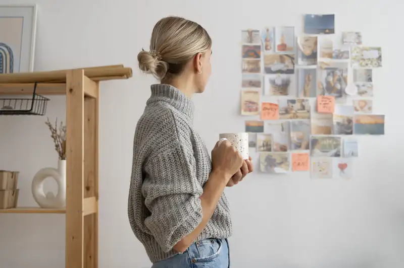 Mulher segurando xícara olhando para vision board na parede