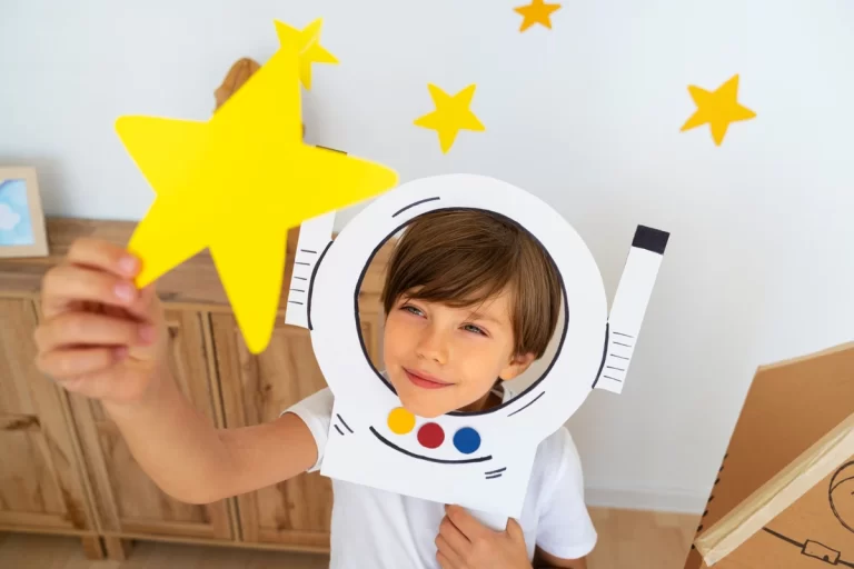 Criança vestindo um traje de astronauta de papel, segurando uma estrela amarela em um ambiente decorado com estrelas.