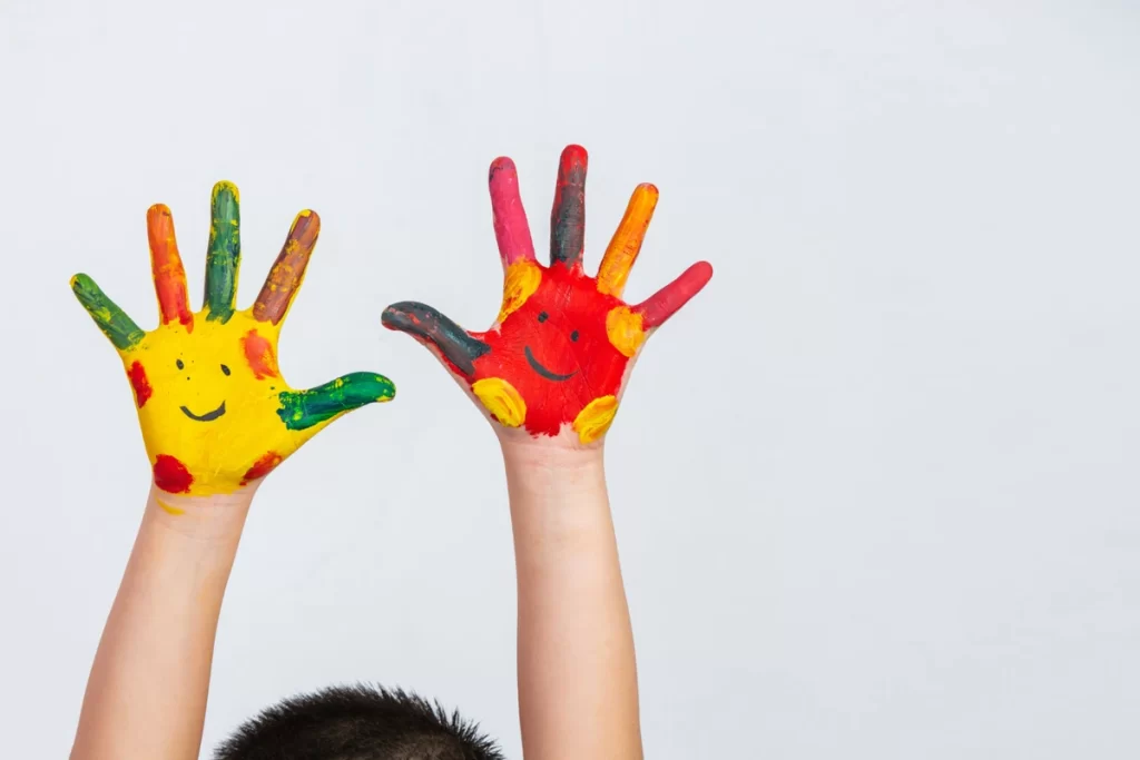 Criança com as mãos pintadas com cores variadas.
