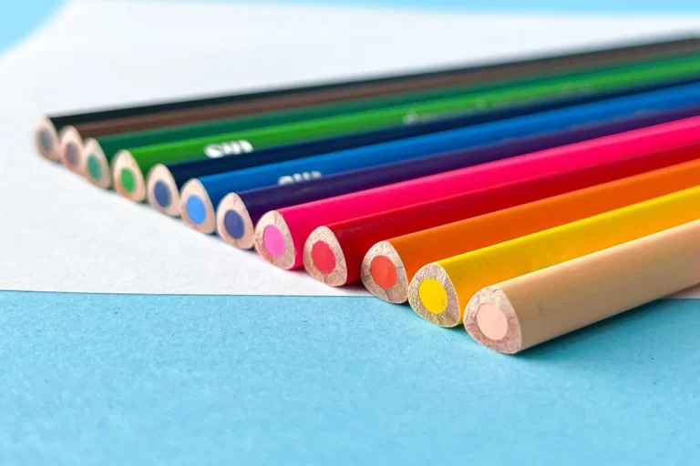 Imagem colorida com itens de papelaria, como lápis de cor, organizados em uma superfície azul.