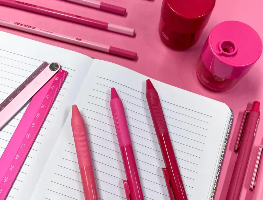 Imagem de materiais de escritório em tons de rosa, incluindo canetas.