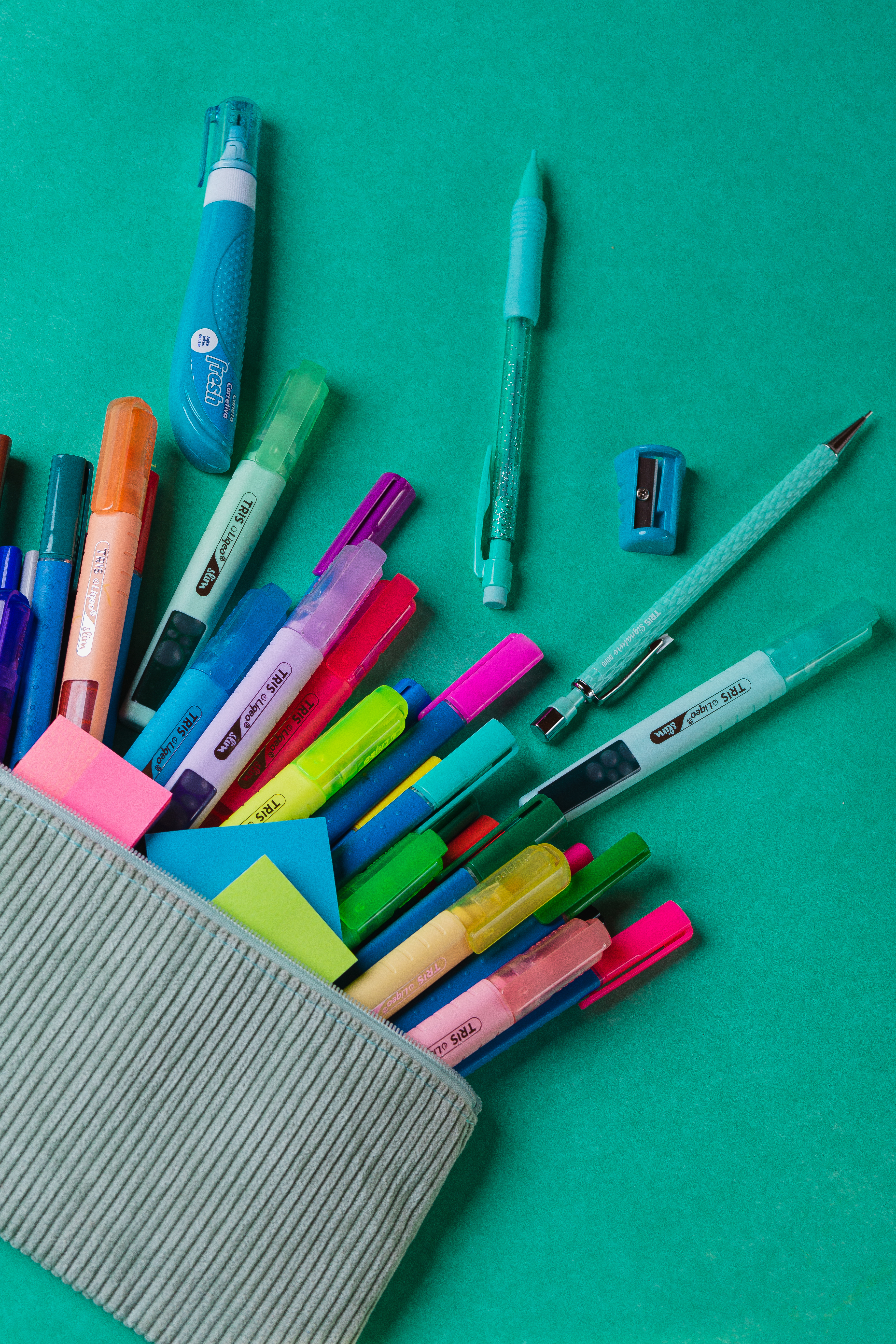 Imagem colorida de canetas, marcadores e post-its dentro de um estojo, em um fundo verde vibrante, ideal para organizar materiais de escrita e estudo.