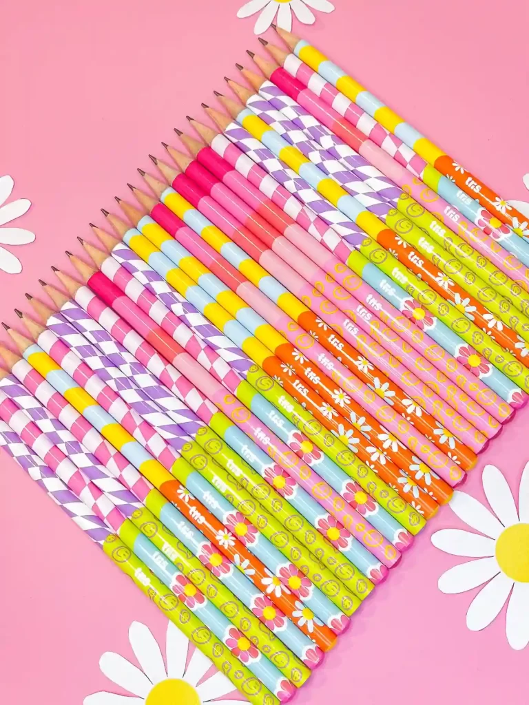 Um conjunto colorido de lápis dispostos em uma superfície rosa, com flores brancas ao fundo, ideal para inspirar criatividade e uso escolar.