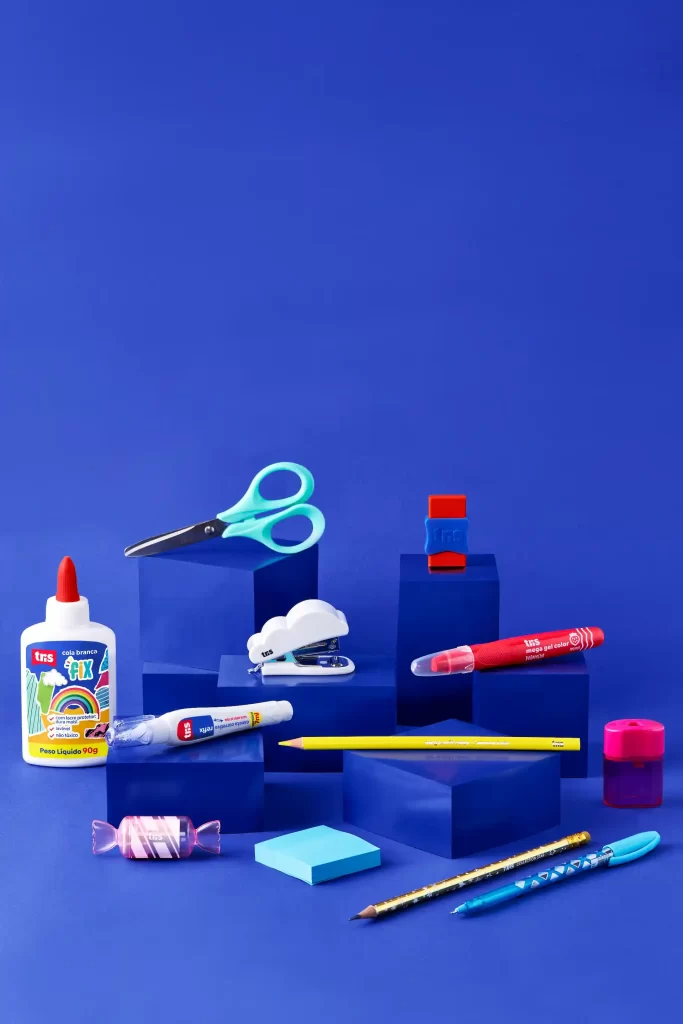 Diversos itens escolares coloridos como cola, tesoura, canetas e blocos de anotações dispostos sobre uma superfície azul, ideal para materiais de papelaria e para quem quer saber como comprar material escolar online.