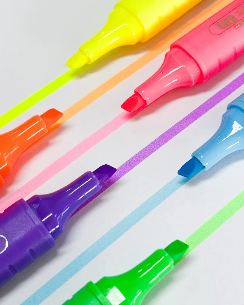 Conjunto de produtos de papelaria com canetas coloridas em tons neon, destacando-se na criação de artes e desenhos vibrantes com cores variadas como amarelo, rosa, azul, verde, roxo e laranja.