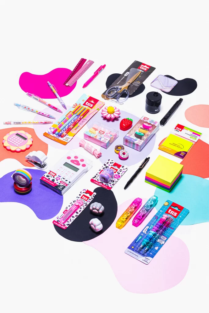 Coleção de papelaria fofa e materiais escolares coloridos para crianças, incluindo canetas, lápis, caderninhos, fitas, esmaltes, e objetos decorativos, sobre uma superfície branca.